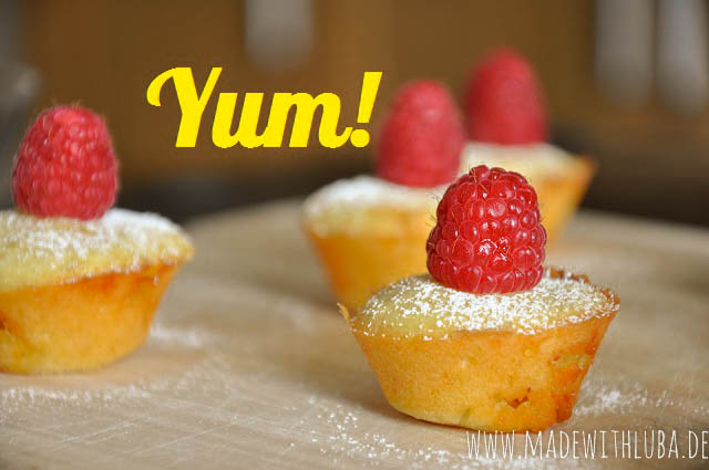 Mini Muffins mit Puderzucker und Himbeeren auf hölzernem Untergrund