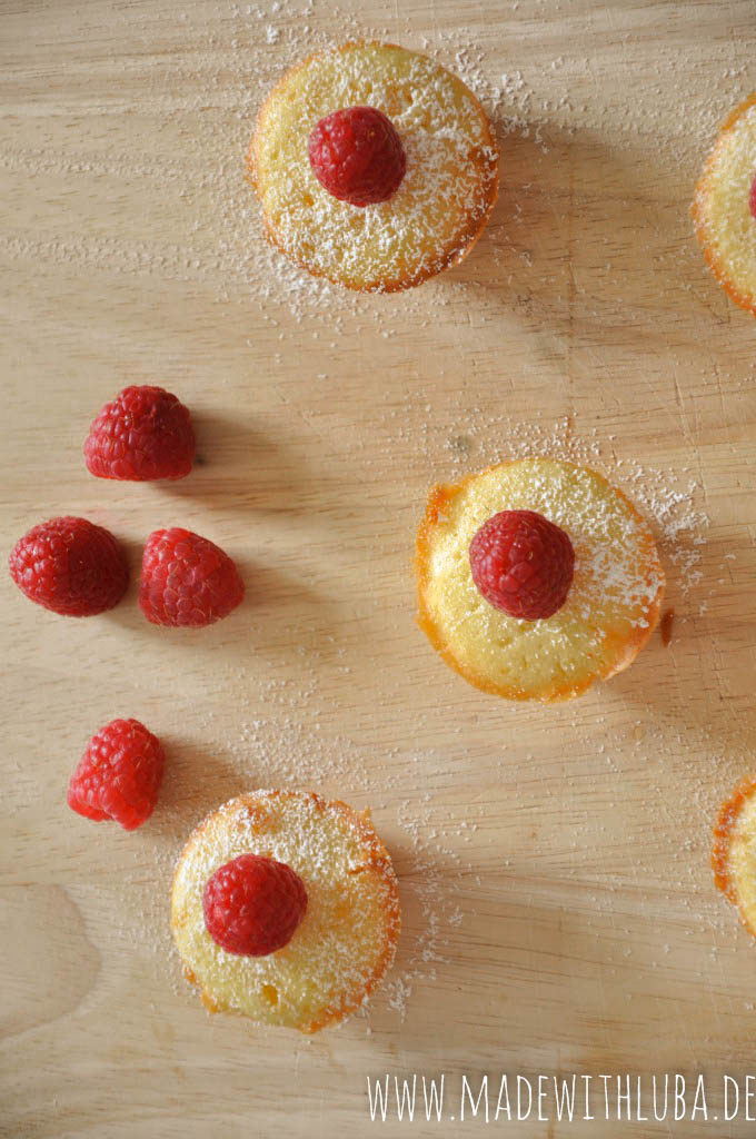 Viele Mini Muffins mit Puderzucker und Himbeeren auf hölzernem Untergrund